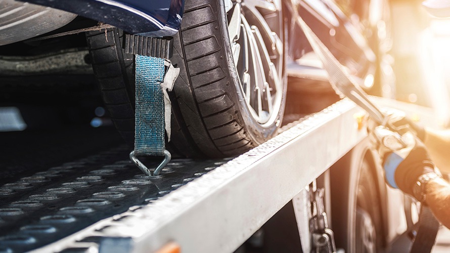 Car on a flatbed tow truck being secured with strap after being recovered with IP AiR Tag